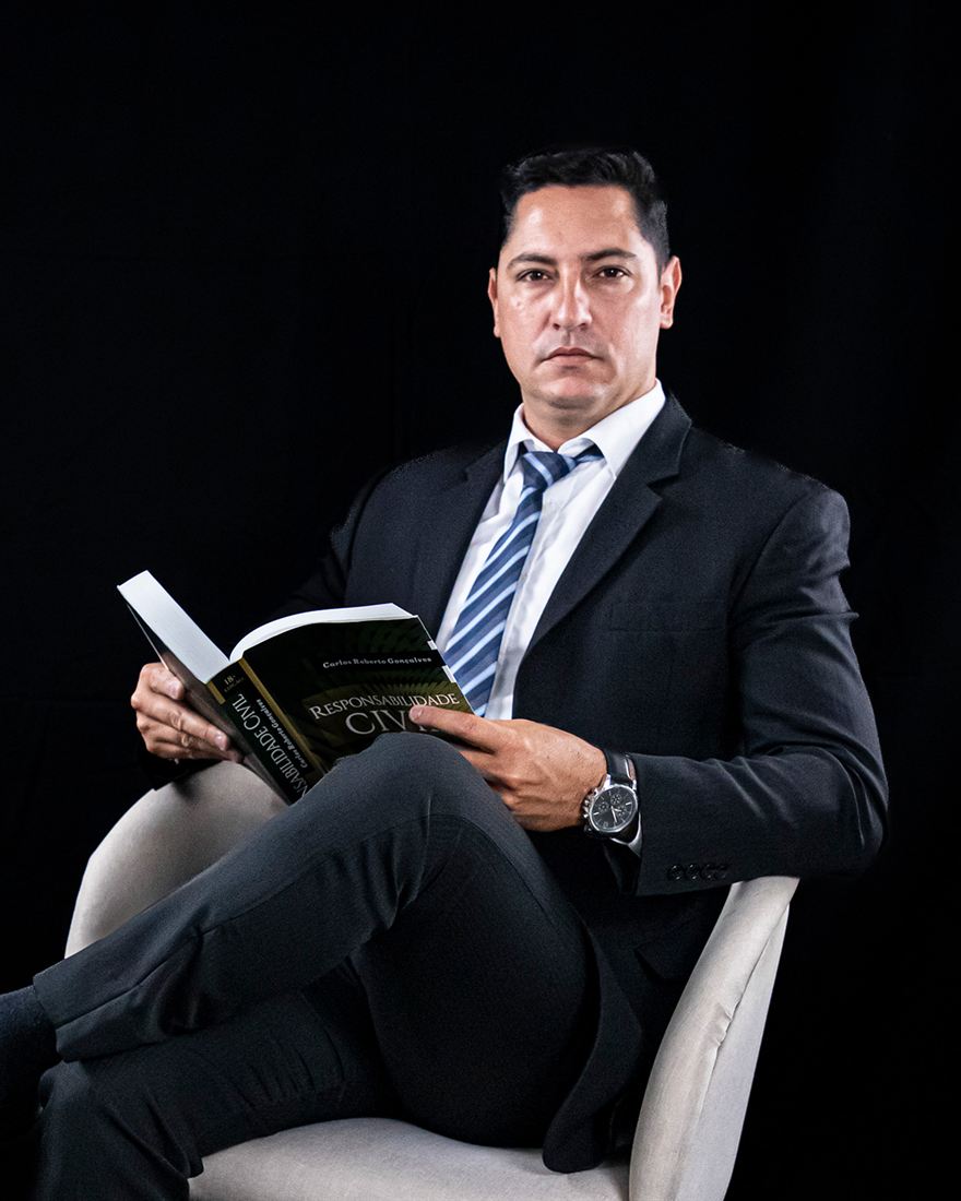 Maicon Mota, da Advocacia Mota, sentado em uma poltrona com um livro de Direito Civil nas mãos